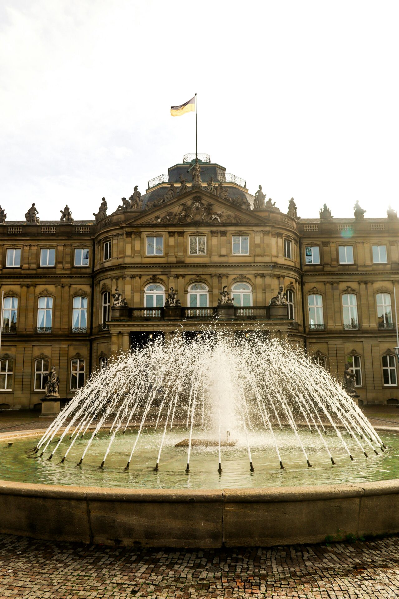 Brunnen im Vordergrund, im Hintergrund das Stuttgarter Schloss mit Deutschlandflagge