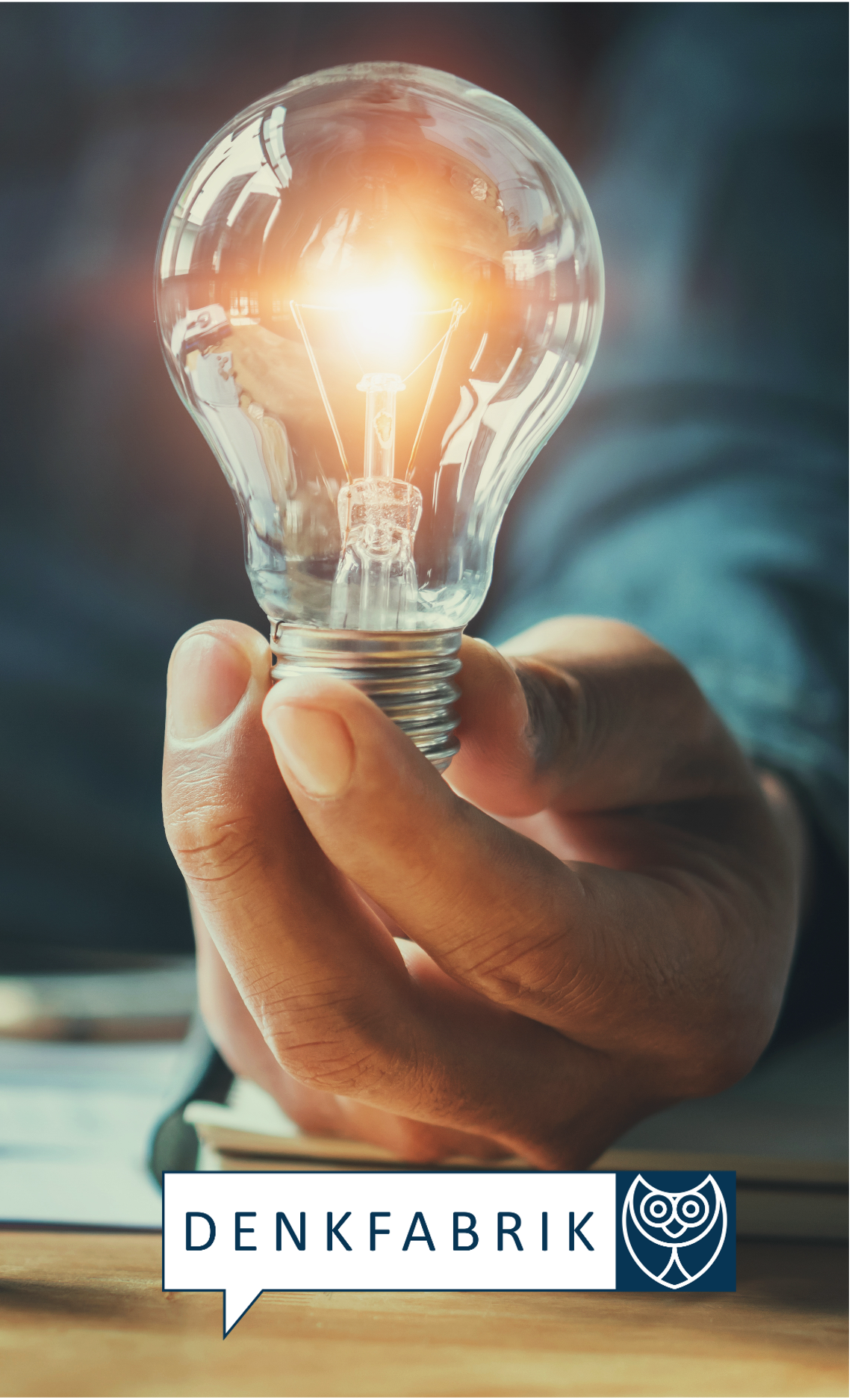 Eine Hand auf Tisch hält eine leuchtende Glühbirne